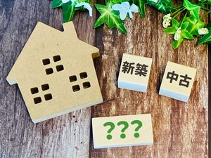 新築と中古の不動産投資を比較するイメージ画像。住宅模型と「新築」「中古」「？」の文字が並んでいる。